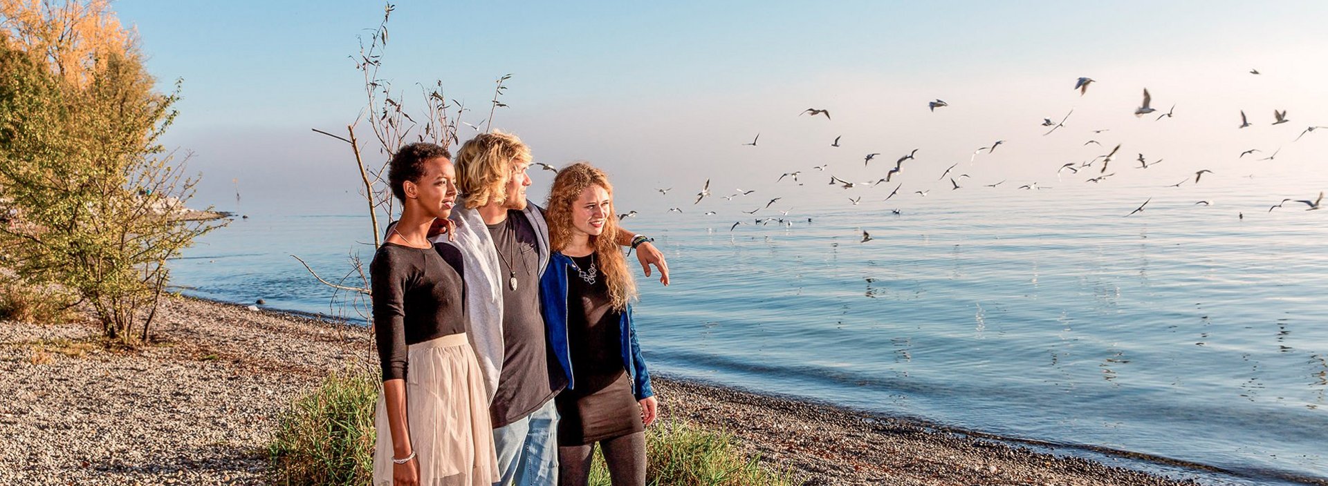 Junge Erwachsene an einem Kiesstrand im Herbst mit Möwen im Hintergrund